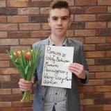 Uczeń SP nr 4 z bukiem tulipanów i planszą z życzeniami: Paniom ze szkoły, babciom, mamom, dziewczynom z klasy i wszystkim damom....