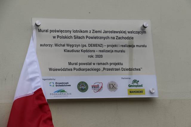 Tablica informacyjna dotycząca muralu usytuowana na budynku szkół przy ul. ś. Ducha 1